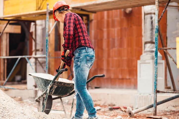 A construction worker puts sand in a wheelbarrow.