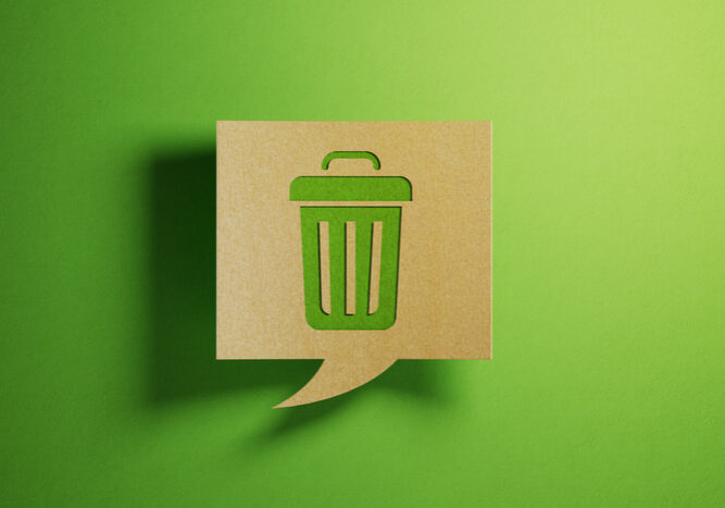 Chat bubble made of recycled paper on green background. There is a trash bin icon on chat bubble. Horizontal composition with copy space.
